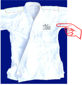 Ein weißer Judogi (Judoanzug) liegt flach auf einem blauen Hintergrund. An der linken Brustseite ist ein Judo-Logo sichtbar, das durch einen Finger verdeutlicht wird, der darauf zeigt.